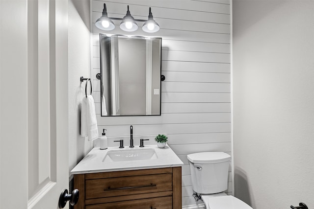 bathroom featuring vanity, wooden walls, and toilet