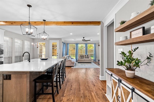 kitchen with wood-type flooring, white cabinetry, a kitchen bar, hanging light fixtures, and a kitchen island with sink