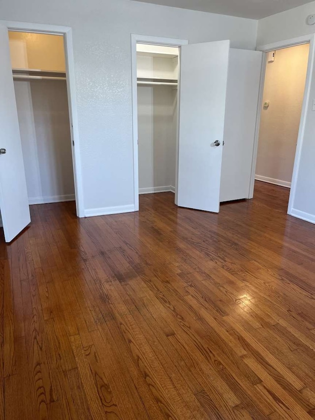 unfurnished bedroom featuring multiple closets and dark wood-type flooring