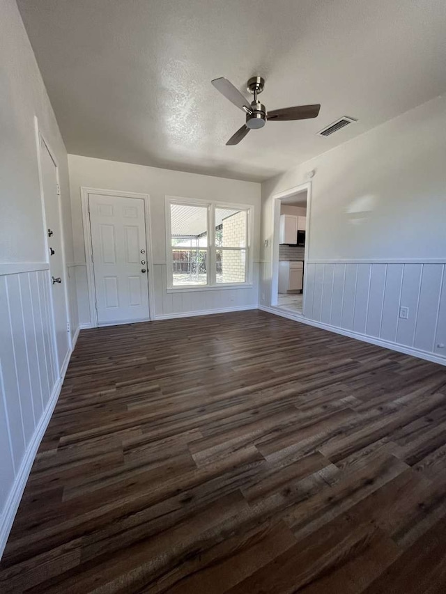 unfurnished living room featuring dark wood-type flooring, a textured ceiling, and ceiling fan