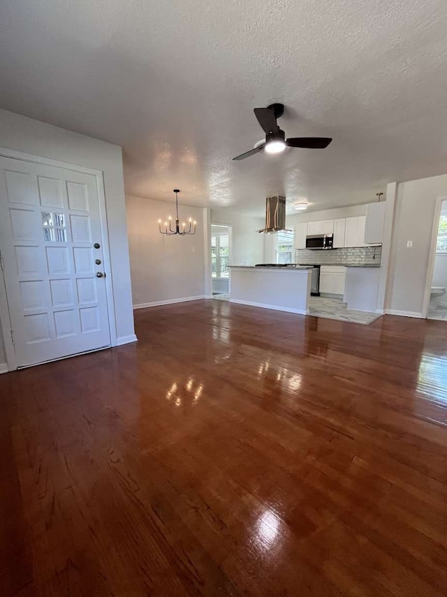 unfurnished living room featuring dark wood-type flooring, a textured ceiling, and ceiling fan with notable chandelier