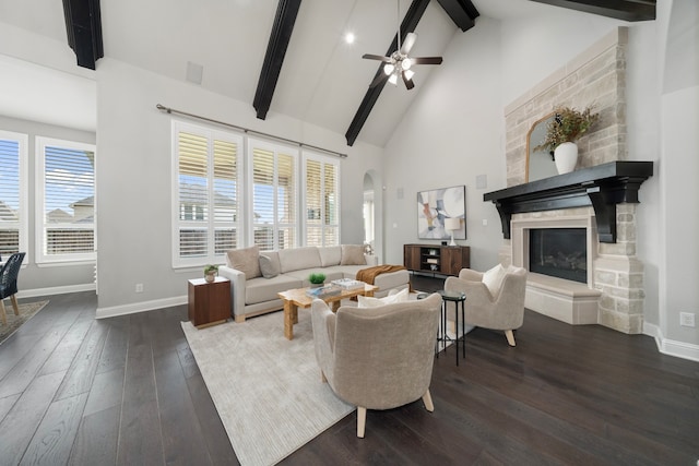 living room featuring a stone fireplace, beamed ceiling, dark wood-type flooring, and a healthy amount of sunlight