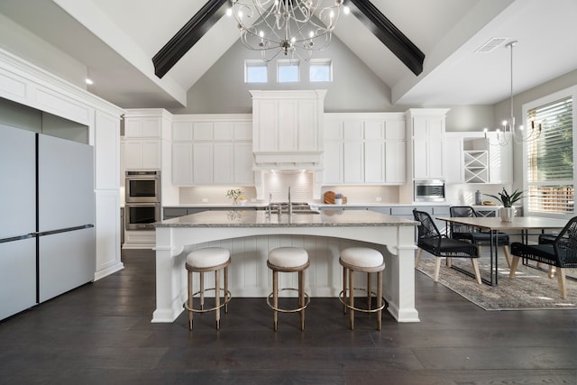 kitchen featuring dark hardwood / wood-style flooring, light stone countertops, white refrigerator, and a center island with sink