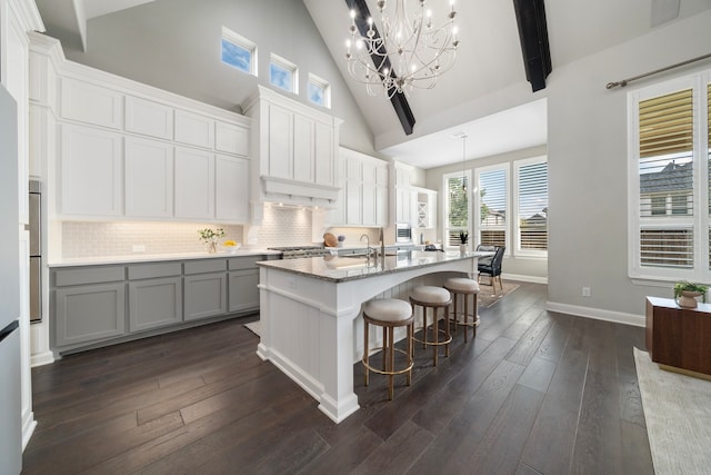 kitchen featuring high vaulted ceiling, hanging light fixtures, a center island with sink, and dark wood-type flooring