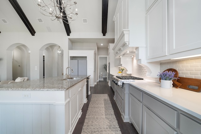 kitchen with white cabinetry, beamed ceiling, sink, and an island with sink