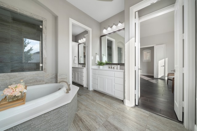 bathroom with hardwood / wood-style flooring, vanity, and a relaxing tiled tub