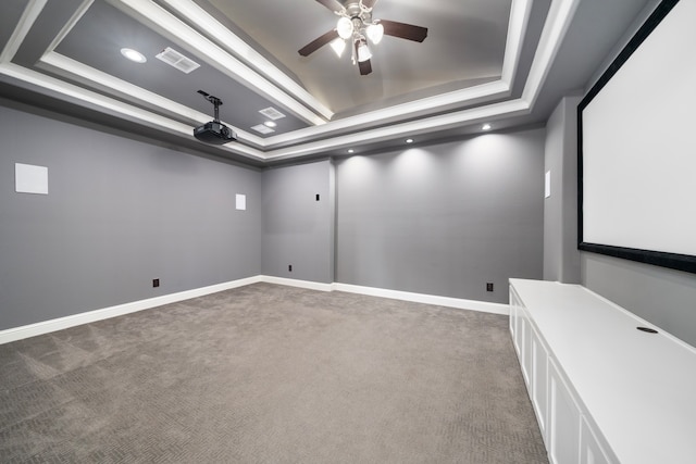 carpeted cinema with ceiling fan and a raised ceiling