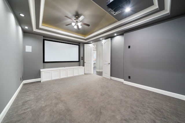 carpeted home theater room featuring a tray ceiling and ceiling fan