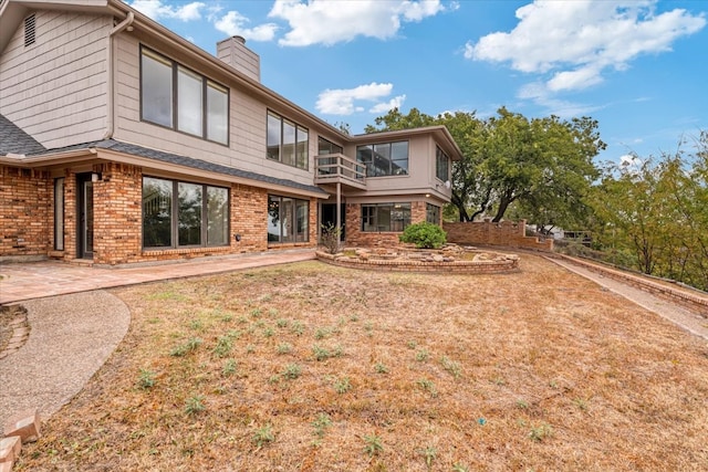 back of house featuring a balcony, a patio, and a lawn