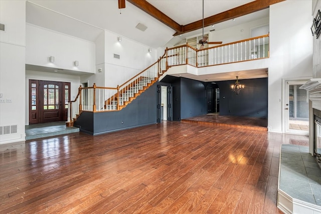 unfurnished living room with ceiling fan with notable chandelier, a fireplace, dark hardwood / wood-style flooring, beamed ceiling, and high vaulted ceiling