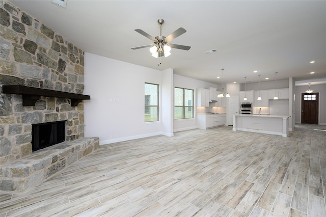 unfurnished living room featuring light hardwood / wood-style floors, a stone fireplace, ceiling fan, and sink