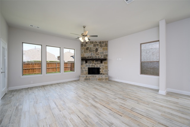 unfurnished living room with light wood-type flooring, a stone fireplace, and ceiling fan