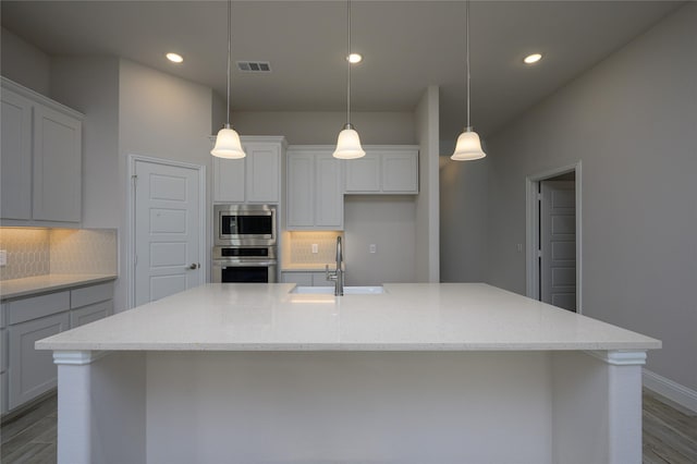 kitchen with decorative backsplash, stainless steel appliances, decorative light fixtures, and an island with sink