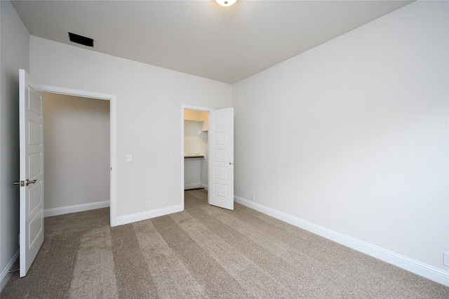 unfurnished bedroom featuring a walk in closet, light carpet, and a closet