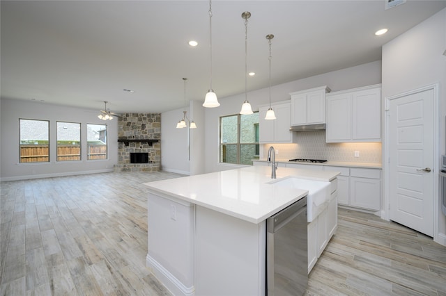 kitchen with a center island with sink, white cabinets, stainless steel dishwasher, a fireplace, and decorative light fixtures