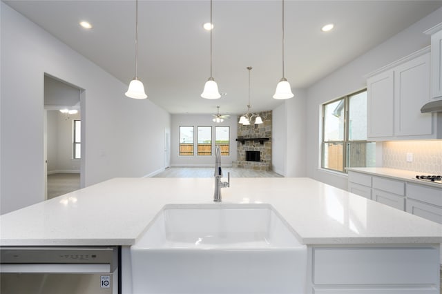 kitchen featuring a fireplace, ceiling fan, a kitchen island with sink, dishwasher, and hanging light fixtures