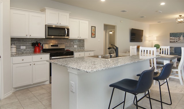 kitchen featuring decorative backsplash, an island with sink, sink, white cabinetry, and appliances with stainless steel finishes