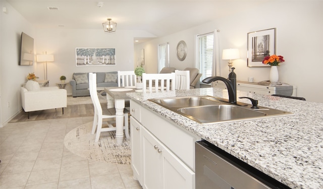 kitchen featuring dishwasher, sink, light stone countertops, light tile patterned floors, and white cabinetry