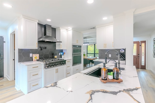 kitchen with wall chimney range hood, light hardwood / wood-style flooring, white cabinets, and stainless steel appliances