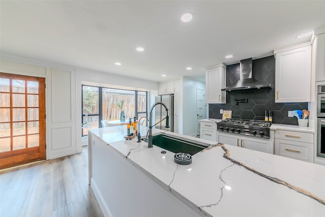 kitchen with light hardwood / wood-style floors, stainless steel appliances, wall chimney range hood, and white cabinets