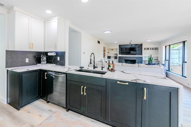 kitchen with white cabinets, light stone counters, stainless steel dishwasher, light wood-type flooring, and sink