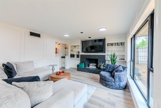 living room with light hardwood / wood-style floors, crown molding, built in features, and a fireplace