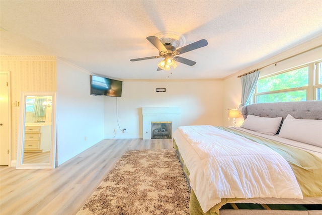 bedroom featuring ceiling fan, a textured ceiling, connected bathroom, ornamental molding, and light hardwood / wood-style floors