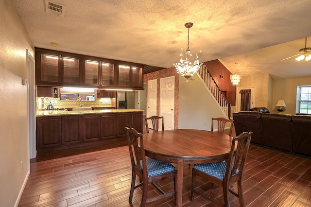 dining space with a textured ceiling, ceiling fan with notable chandelier, and dark wood-type flooring