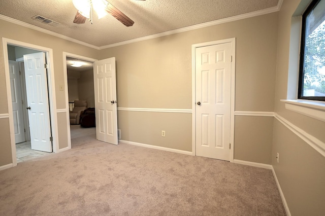 unfurnished bedroom featuring ceiling fan, light colored carpet, a textured ceiling, and crown molding