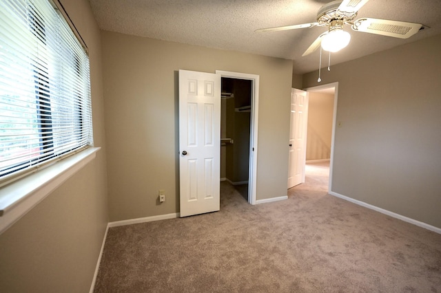 unfurnished bedroom featuring ceiling fan, a textured ceiling, a walk in closet, light carpet, and a closet