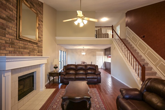 living room with hardwood / wood-style floors, ceiling fan, a towering ceiling, and a tiled fireplace