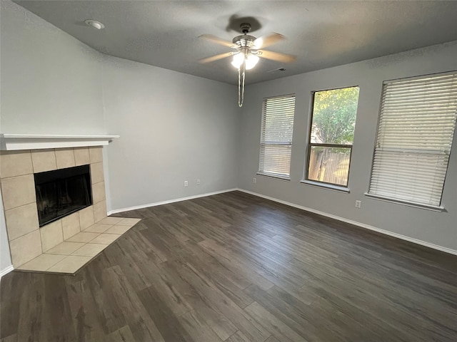 unfurnished living room featuring dark hardwood / wood-style floors, a tiled fireplace, a textured ceiling, and ceiling fan