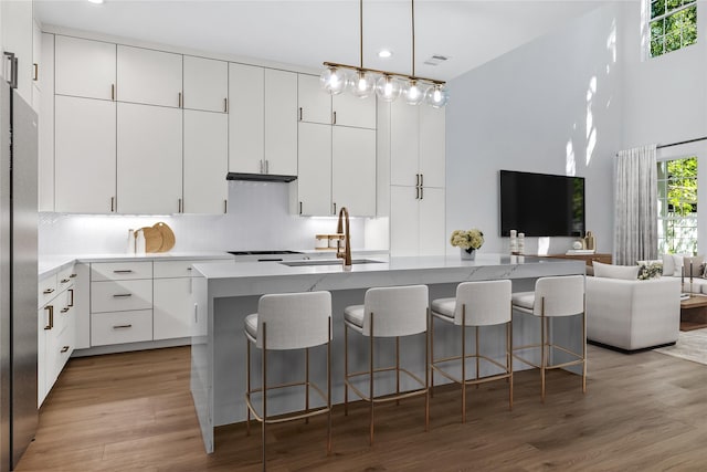 kitchen with backsplash, sink, an island with sink, light hardwood / wood-style floors, and white cabinetry