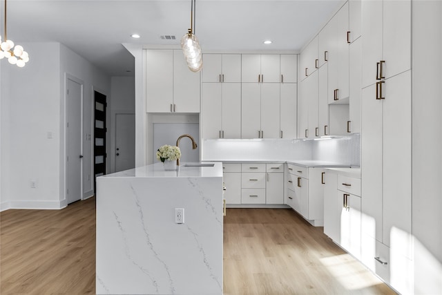 kitchen with white cabinets, pendant lighting, an island with sink, and sink