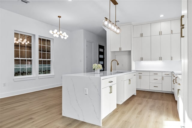 kitchen with light wood-type flooring, a kitchen island with sink, sink, white cabinetry, and hanging light fixtures