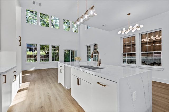 kitchen with a kitchen island with sink, sink, light hardwood / wood-style floors, light stone counters, and white cabinetry