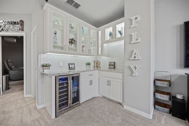 bar featuring light colored carpet, light stone counters, beverage cooler, white cabinets, and backsplash