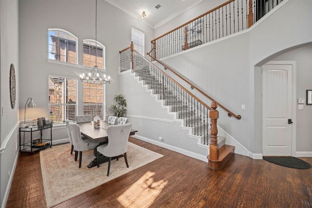 dining area featuring ornamental molding, a towering ceiling, dark wood-type flooring, and a notable chandelier