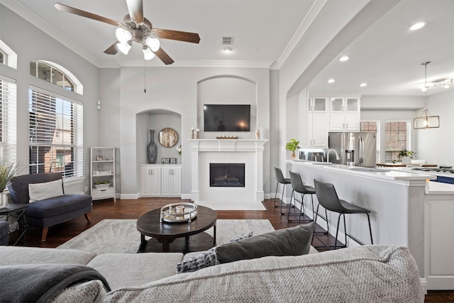 living room with ceiling fan, dark hardwood / wood-style floors, a tiled fireplace, and ornamental molding