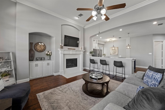 living room featuring ornamental molding, a tiled fireplace, dark hardwood / wood-style floors, and ceiling fan