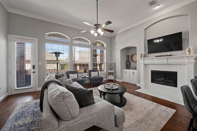 living room with dark wood-type flooring, ceiling fan, a tile fireplace, and ornamental molding