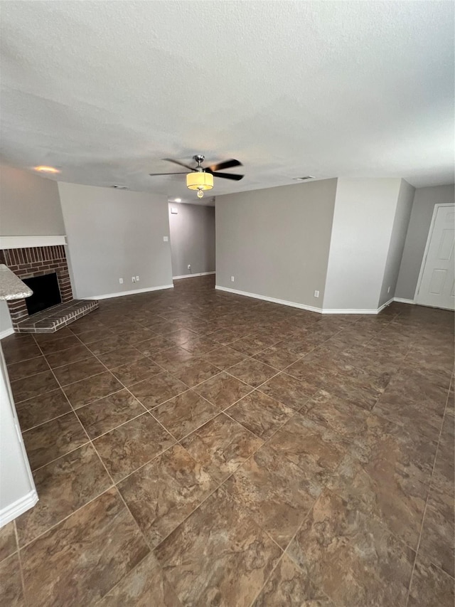 unfurnished living room featuring ceiling fan, a textured ceiling, and a brick fireplace