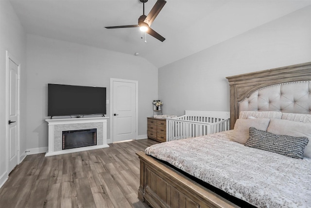 bedroom featuring a stone fireplace, ceiling fan, lofted ceiling, and hardwood / wood-style flooring