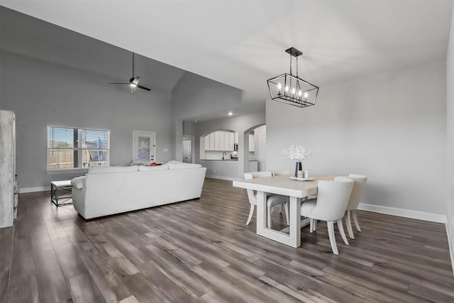 dining area with ceiling fan with notable chandelier, dark hardwood / wood-style floors, and high vaulted ceiling