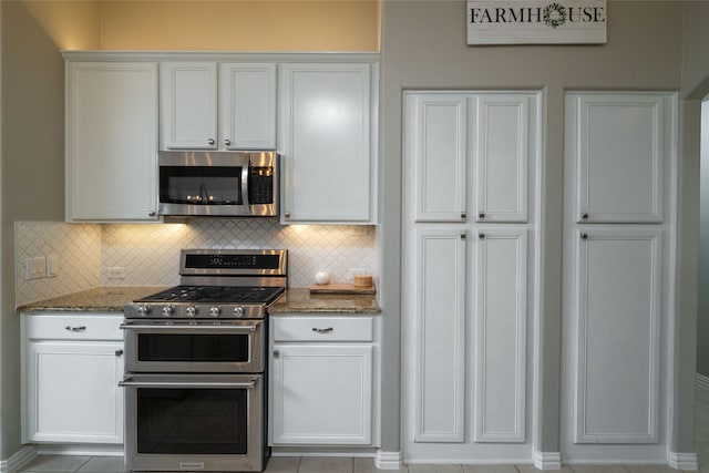 kitchen with decorative backsplash, white cabinets, dark stone countertops, light tile patterned flooring, and stainless steel appliances