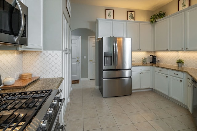 kitchen with white cabinets, light tile patterned floors, backsplash, light stone countertops, and stainless steel appliances