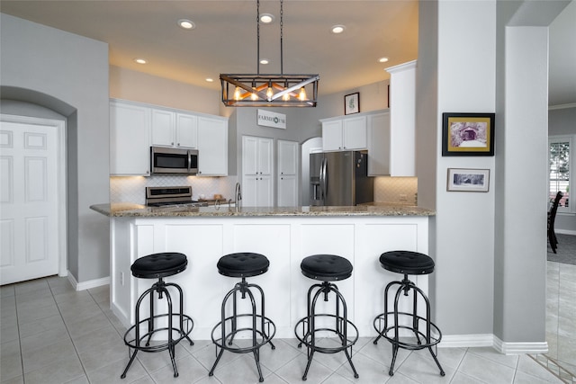 kitchen with kitchen peninsula, backsplash, white cabinetry, light stone countertops, and stainless steel appliances