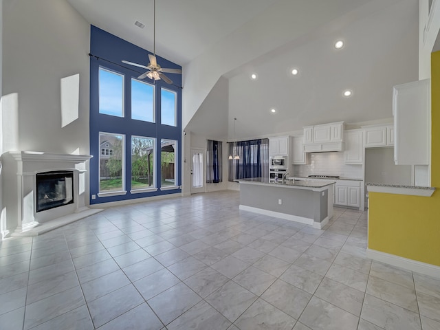 kitchen with white cabinets, ceiling fan, a towering ceiling, an island with sink, and light tile patterned floors