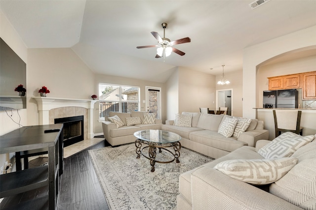 living room with ceiling fan with notable chandelier, vaulted ceiling, a tile fireplace, and dark hardwood / wood-style floors