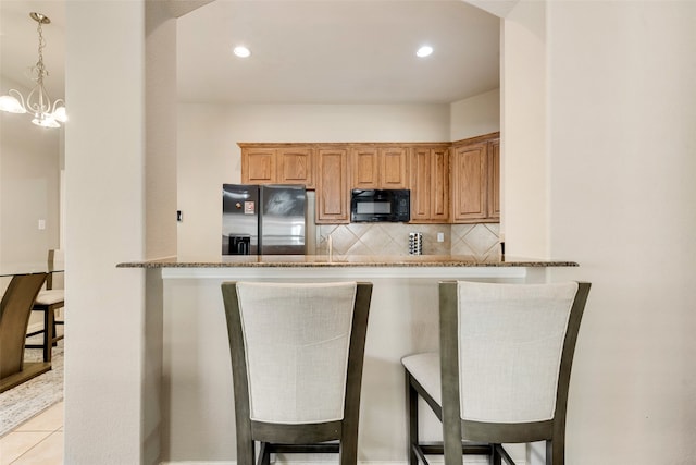 kitchen with light tile patterned flooring, black appliances, a kitchen bar, and pendant lighting